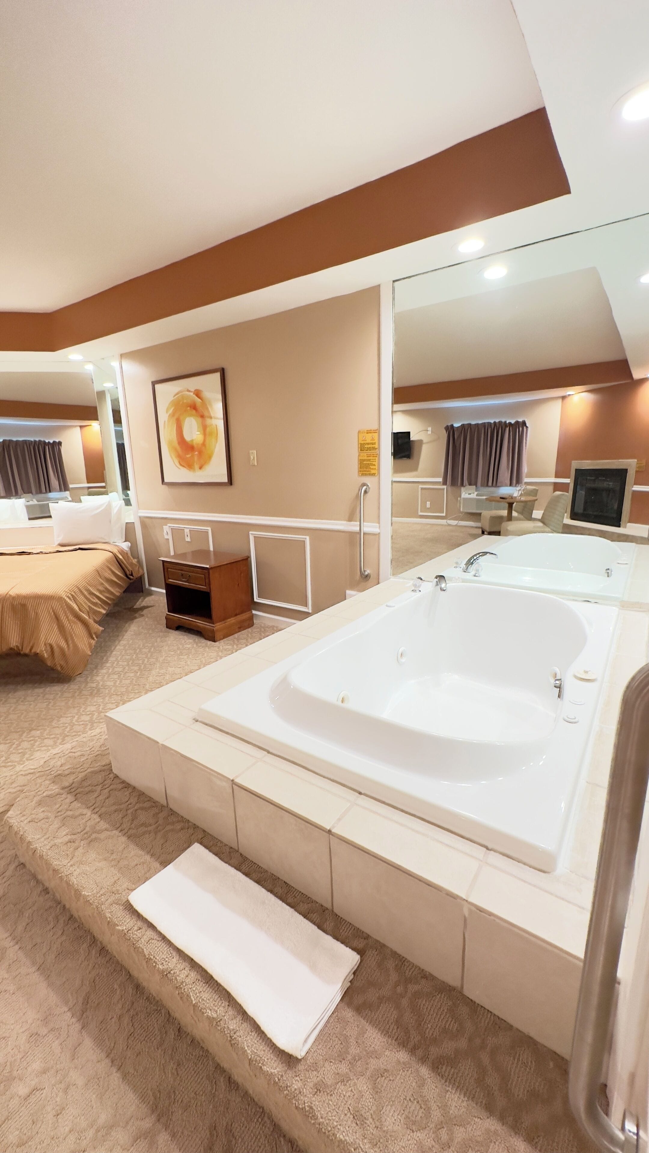 A modern bathroom with a large bathtub, a mirror, and a small bedside table.