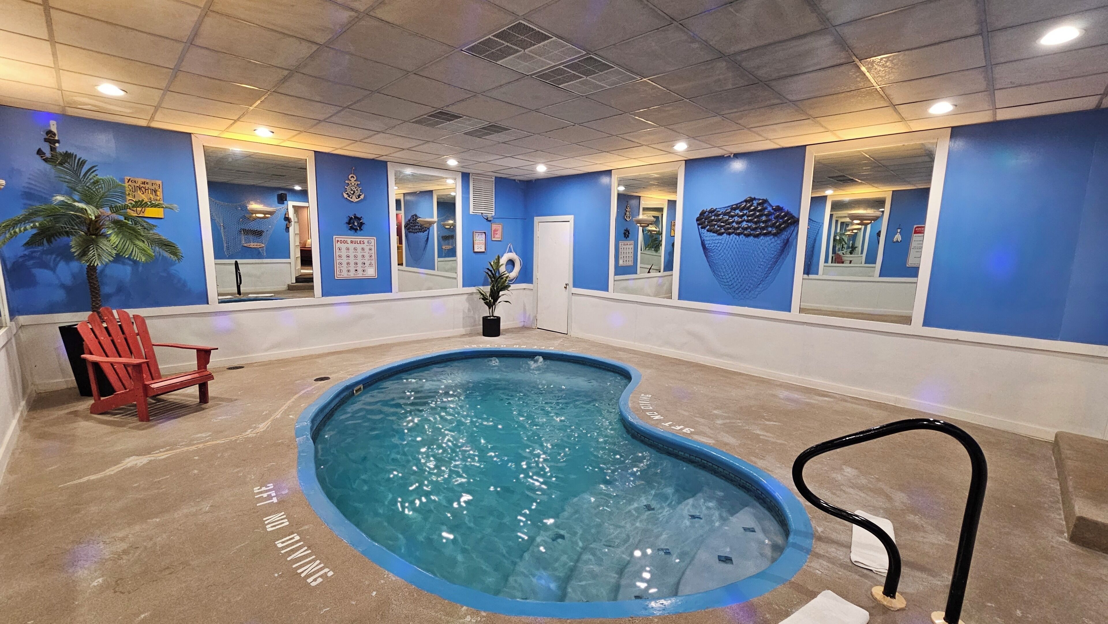 An indoor swimming pool with blue walls, a red chair, and a pool rule sign.