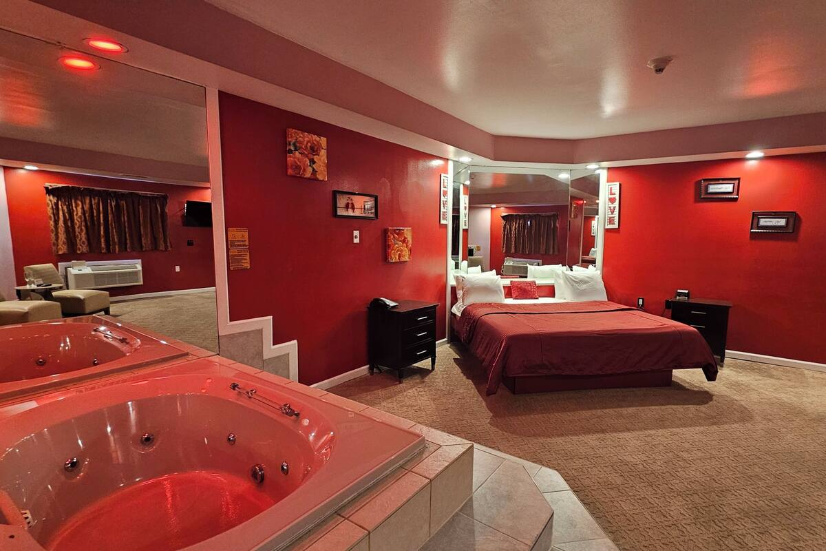 Une pièce avec un grand jacuzzi aux carreaux rouges, un lit avec une literie rouge, un miroir et un mur rouge.