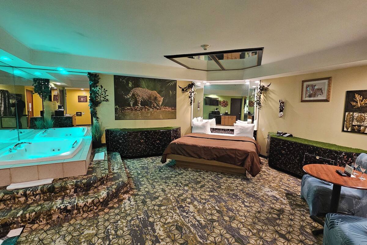 Une chambre d’hôtel avec un grand lit, un coin salon avec un canapé, une petite table et un jacuzzi.