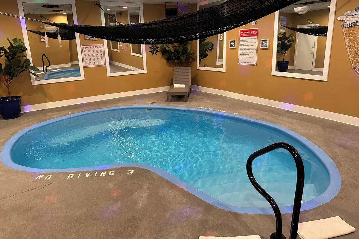 Une piscine intérieure avec un espace dédié aux plongeons, un panneau affichant les règles de la piscine et un hamac.