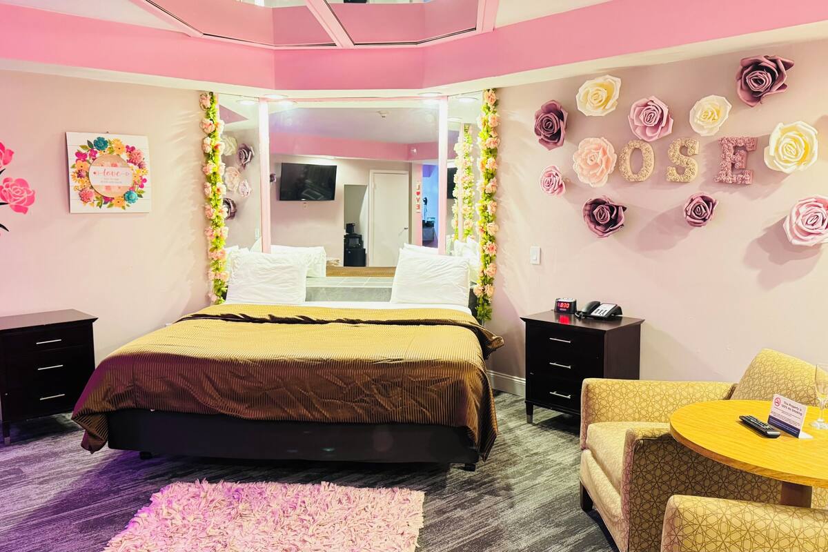 Une chambre à coucher comprenant un lit, des tables de chevet, un miroir, une chaise et une petite table sur laquelle se trouvent un téléphone et une horloge.