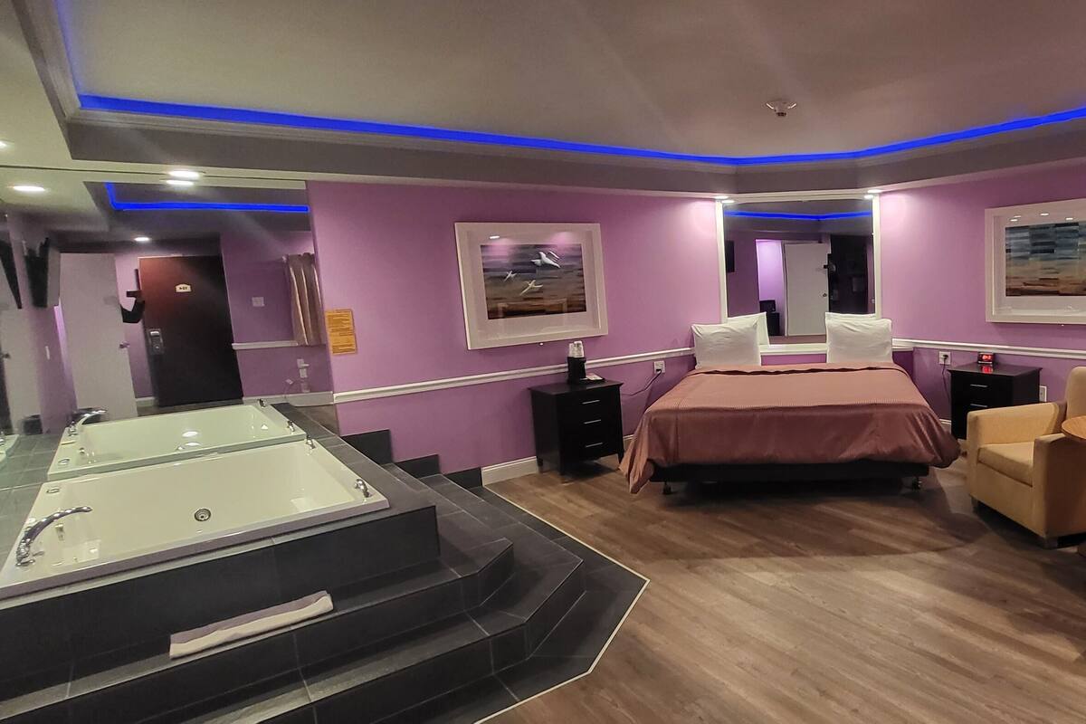 Une chambre d’hôtel avec un grand lit, un coin salon avec deux fauteuils, une petite table ronde, une cheminée et une grande baignoire.