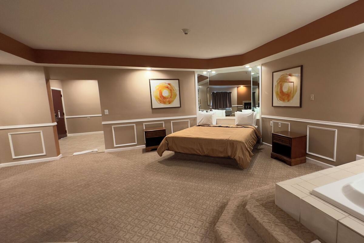 Une chambre d’hôtel dotée d’un grand lit, d’une salle de bain séparée avec baignoire, d’une coiffeuse avec miroir et d’œuvres d’art accrochées aux murs.