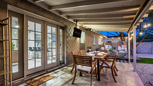 An outdoor patio with a dining table and chairs, a TV mounted on the wall, and a doormat on the door. - Quiet Oasis in Old Town Scottsdale (Scottsdale)