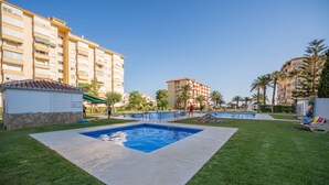 A swimming pool surrounded by well-maintained grass, with multi-story buildings in the background. - Estudio Medayra by Solset (Torrox)