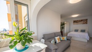 A modern apartment with a grey sofa, a white bed, and a balcony with a potted plant. - Estudio Medayra by Solset (Torrox)