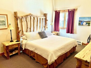 Une chambre à coucher avec une tête de lit en bois, un lit avec une literie blanche, une table de chevet avec une lampe et une fenêtre avec des rideaux.
