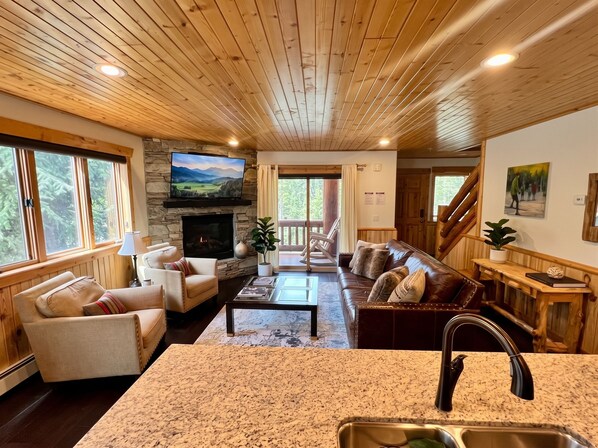 A cozy living room with a stone fireplace, a television, and a large window.