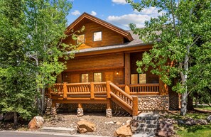 A wooden cabin with a porch, stone steps, and a view of the surrounding trees.