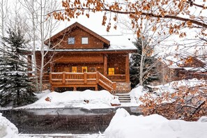 A wooden cabin with a porch, surrounded by snow-covered ground and trees.