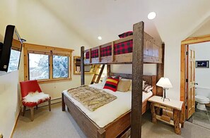 Habitación con literas, un escritorio, una silla, una ventana con vistas a árboles y un baño con puerta de madera.