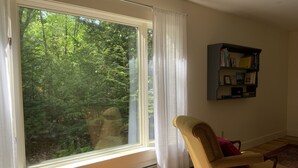 Et værelse med et stort vindue, en radiator, en stol og en bogreol.