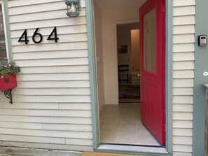 Uma casa com o número 464 na lateral, uma porta vermelha e um pequeno candeeiro exterior.