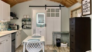 A compact kitchen with a white table, a white chair, a black hanging rack, and a white cabinet. - Tiny for Two + Small Dog OK! -  Near BEACH, SPORTS COMPLEX, OWA, TANGER (Foley)