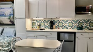 A compact kitchen with white cabinets, a stainless steel refrigerator, a coffee maker, and a kettle on the counter. - Tiny for Two + Small Dog OK! -  Near BEACH, SPORTS COMPLEX, OWA, TANGER (Foley)