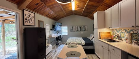 Ein kleines Schlafzimmer mit Bett, Schreibtisch und Stuhl, eine Küchenzeile mit Schränken und Spüle sowie eine Holzboden.