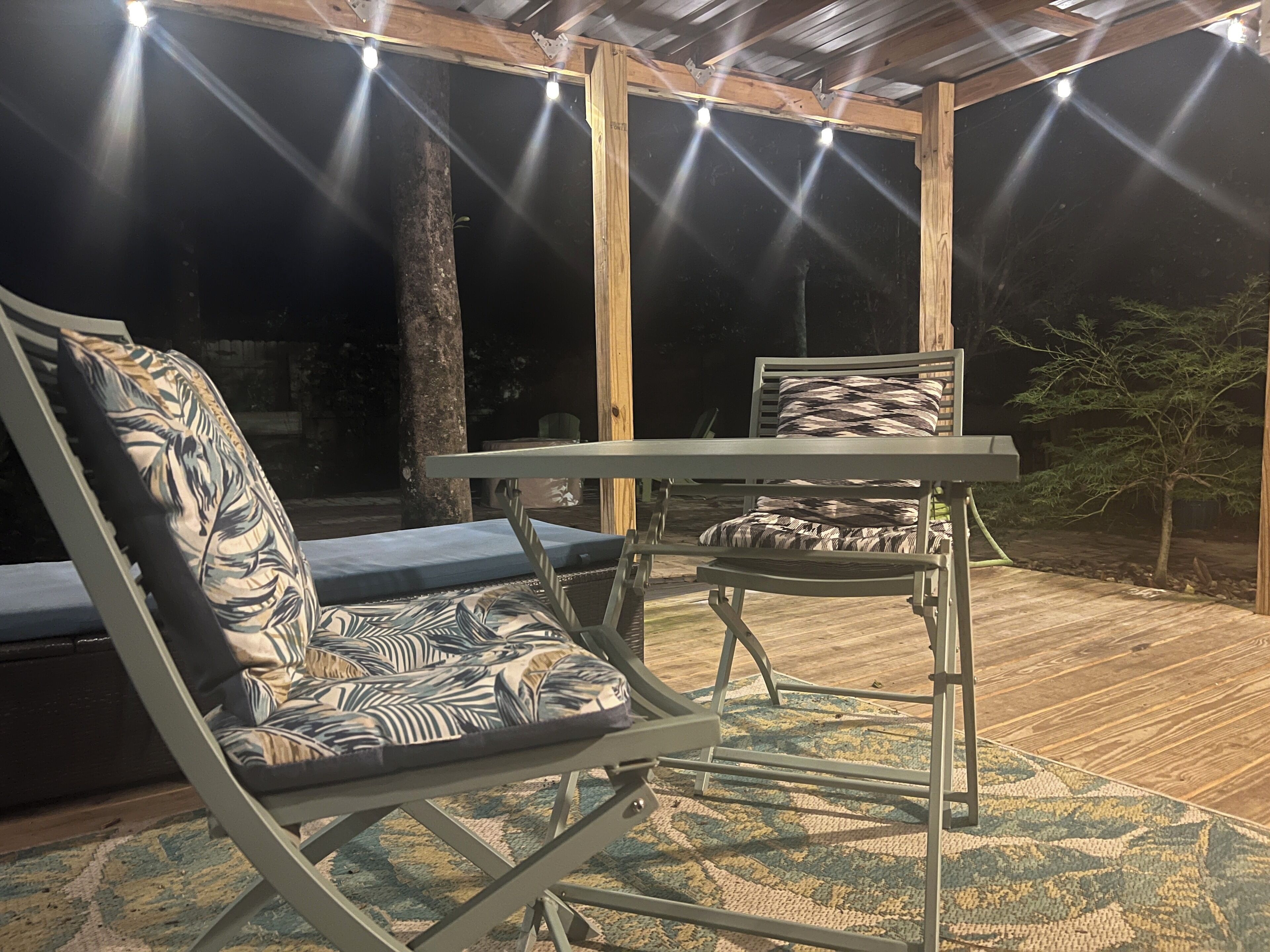 An outdoor seating area with a table and chairs, a patterned cushion, and a wooden deck.