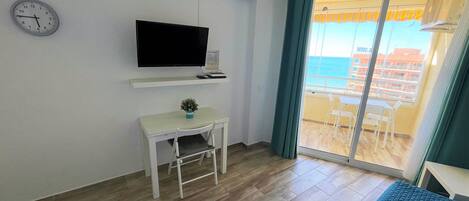 A room with a bed, a desk with a chair, a television, and a view of the sea through a sliding door.