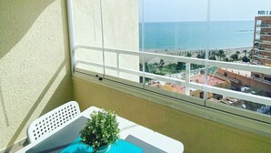 Un balcon avec vue sur la mer, une petite table avec une plante et une chaise.