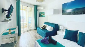 Une chambre d’hôtel avec un lit, un bureau, une chaise, une télévision et une vue sur la mer.