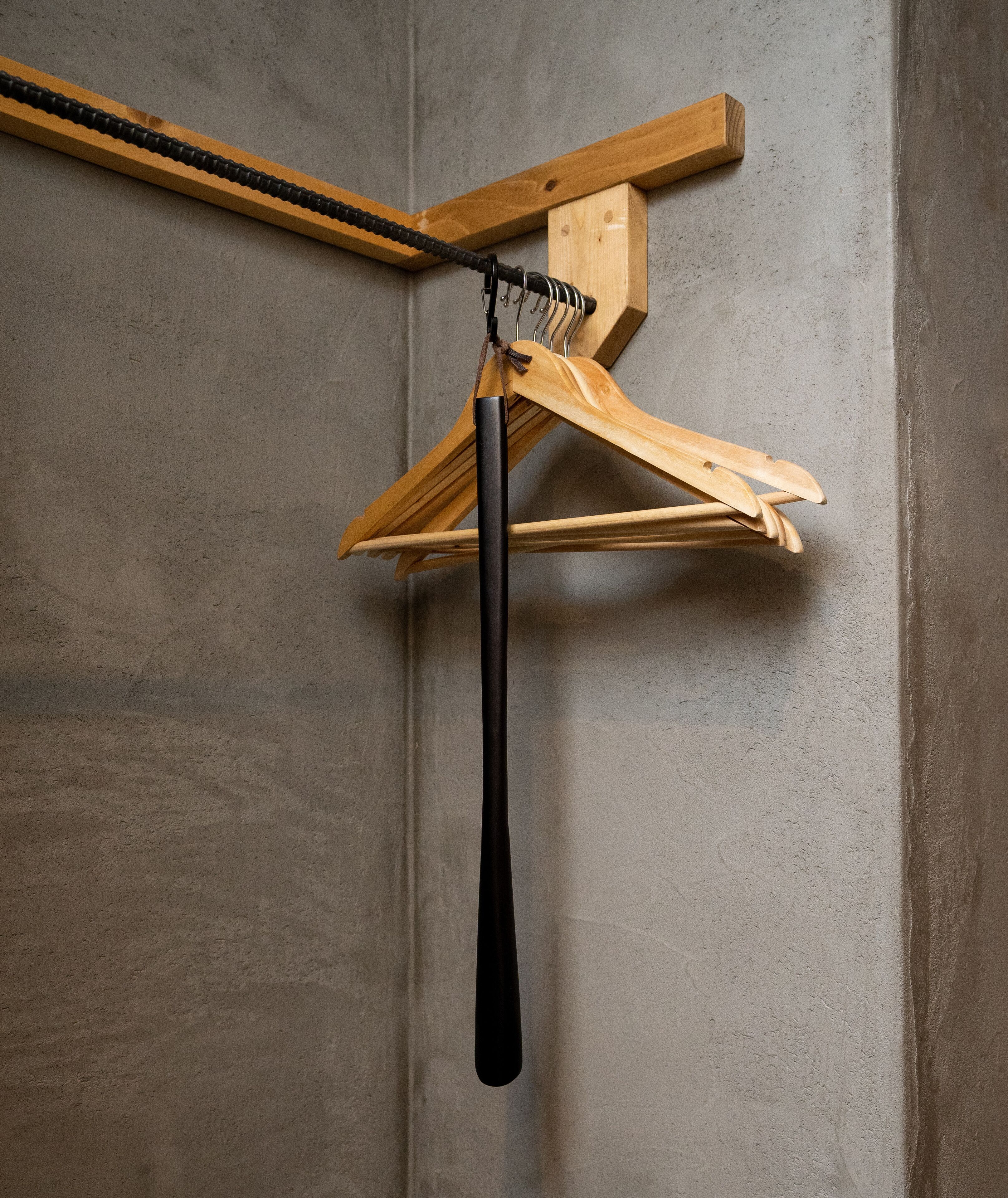 Un porte-manteau en bois avec un cintre noir, adossé à un mur en béton.