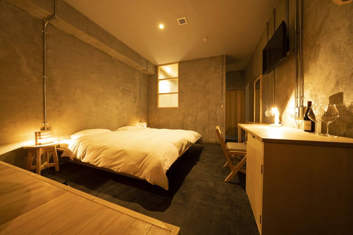 Un dormitorio moderno con cama, mesita de noche, lámpara y una pequeña silla de madera.