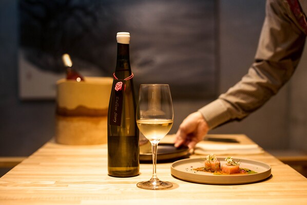 A bottle of wine, a wine glass, and a plate with food on a wooden table. - Yoichi LOOP (Yoichi)