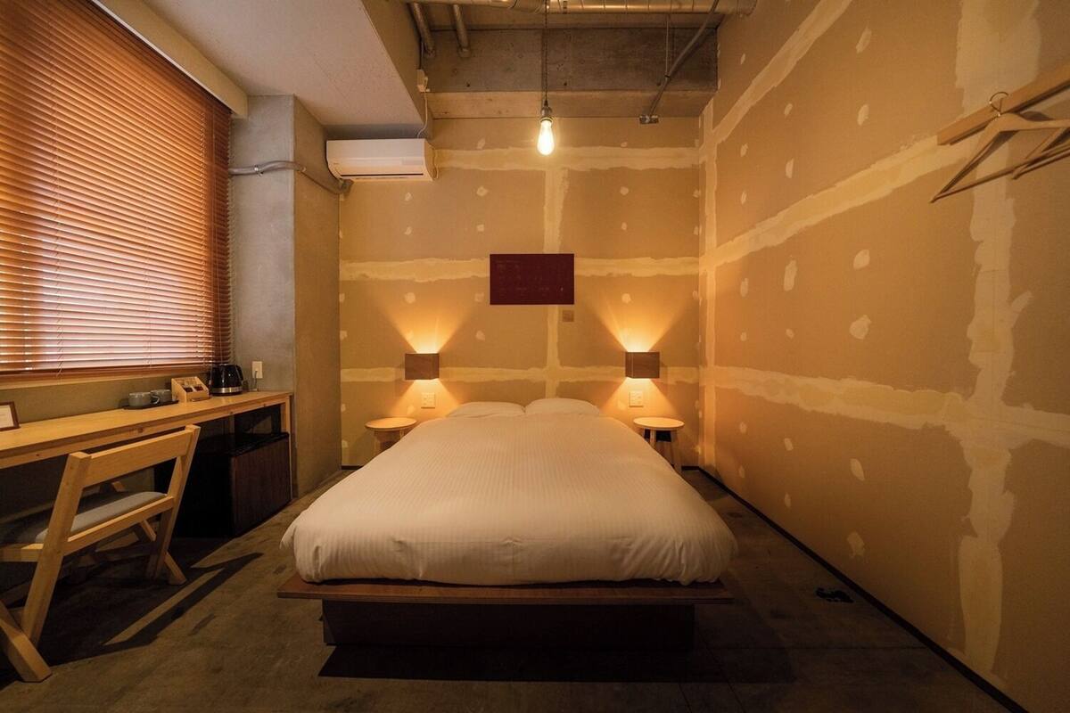 Un dormitorio con cama, lámparas de noche, escritorio y ventana con persianas.