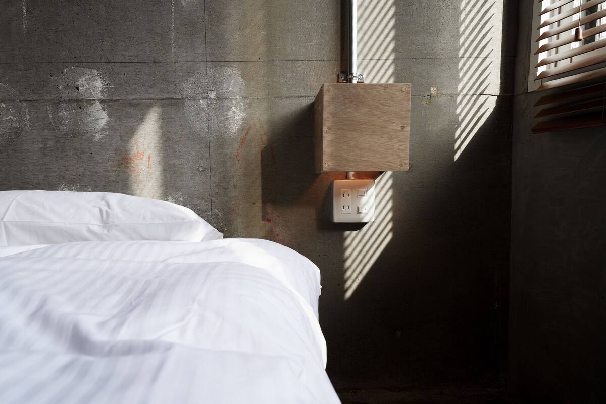 Una cama en una habitación con pared de concreto y una caja de madera fijada a ella.