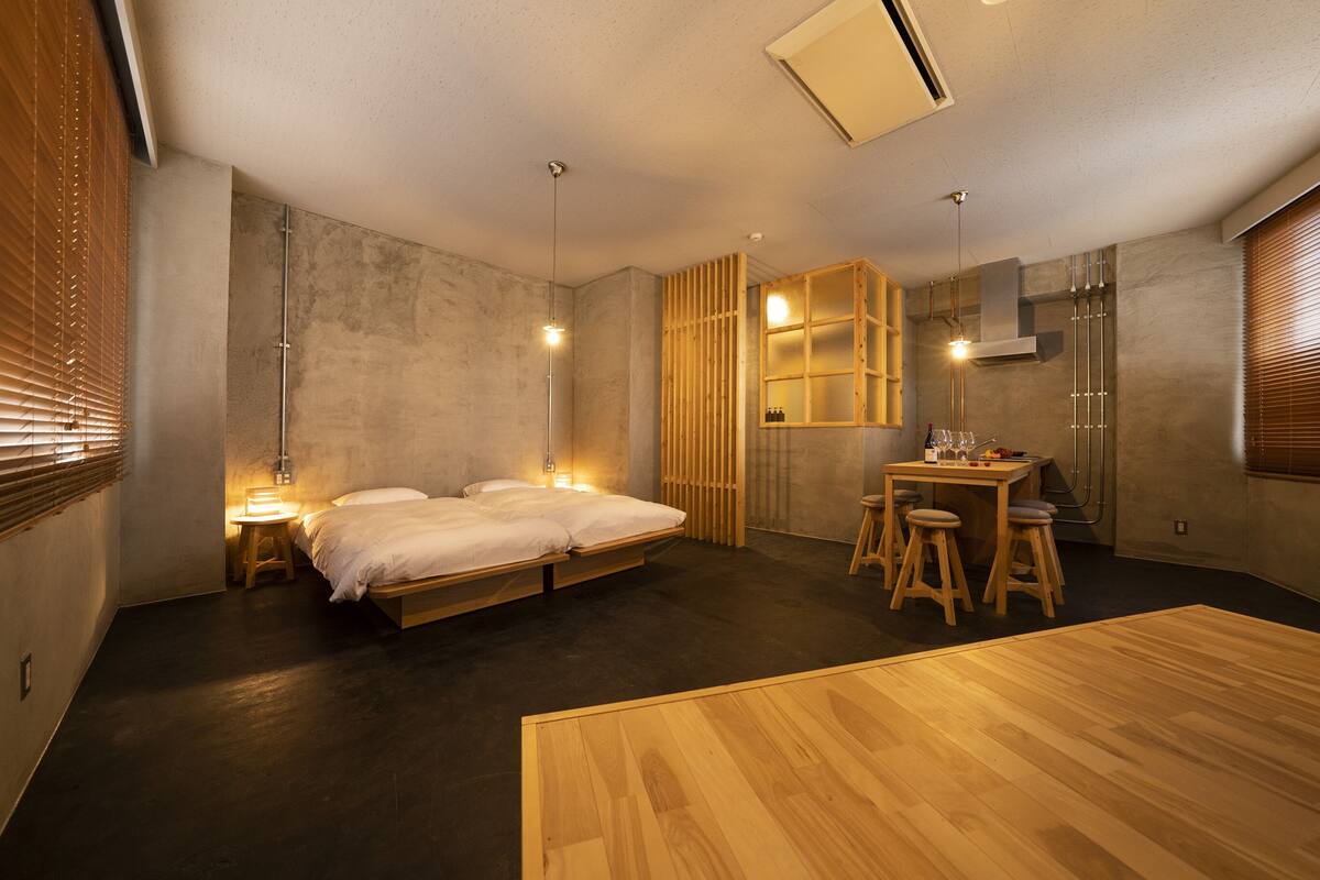 Un dormitorio moderno con una cama grande, un escritorio pequeño con taburetes y una mesa de madera.