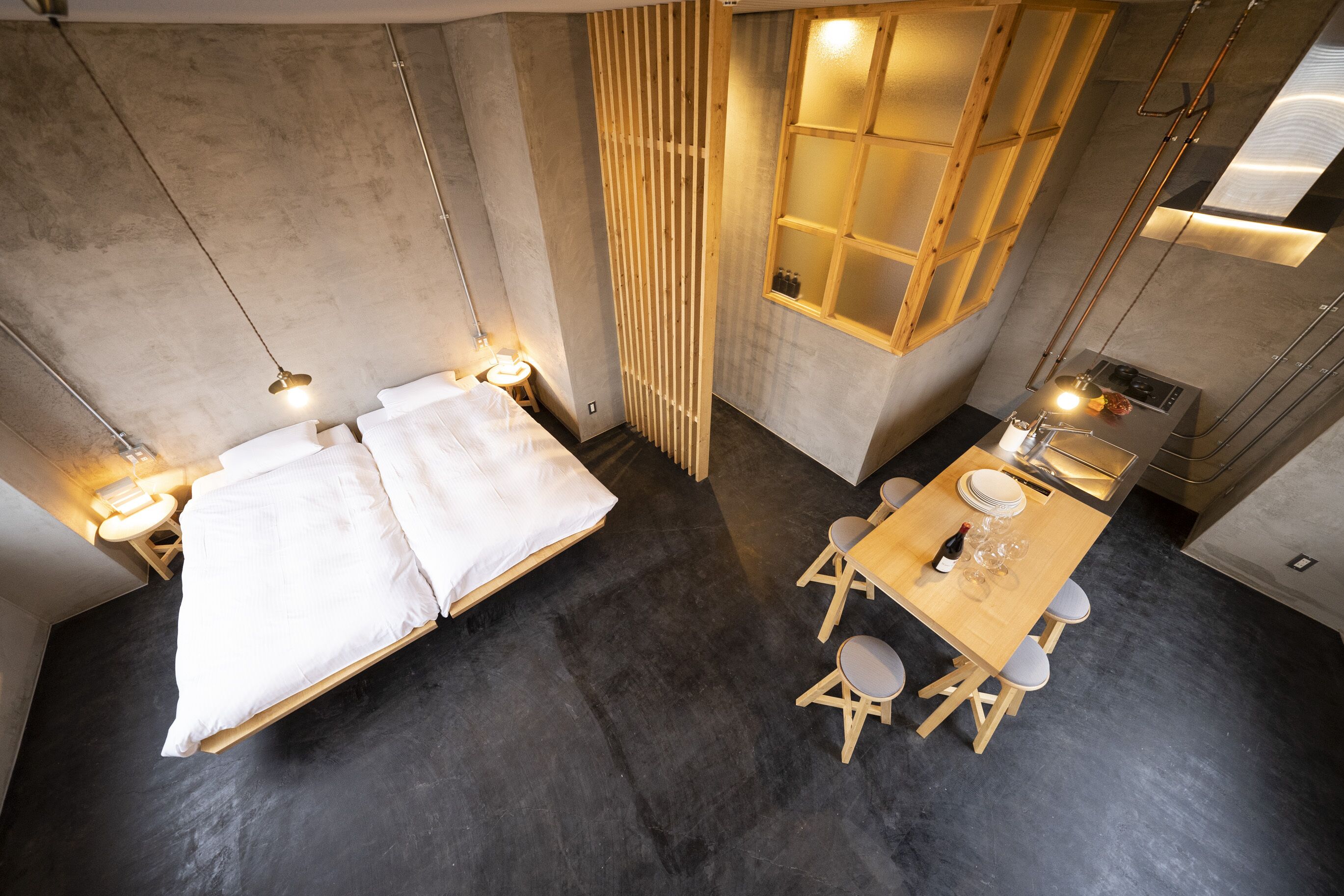 A compact room with a bed, a dining table with chairs, a small kitchen area, and a window with blinds.