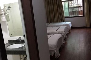 Habitación de hotel con piso de madera, ventana con cortinas, lavamanos con espejo y dos camas con ropa blanca.