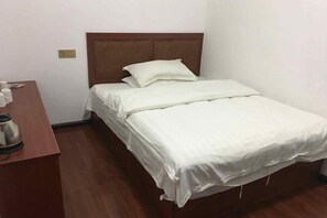 Una cama individual con cabecera de madera, una mesita de noche de madera con una tetera y una pared blanca.