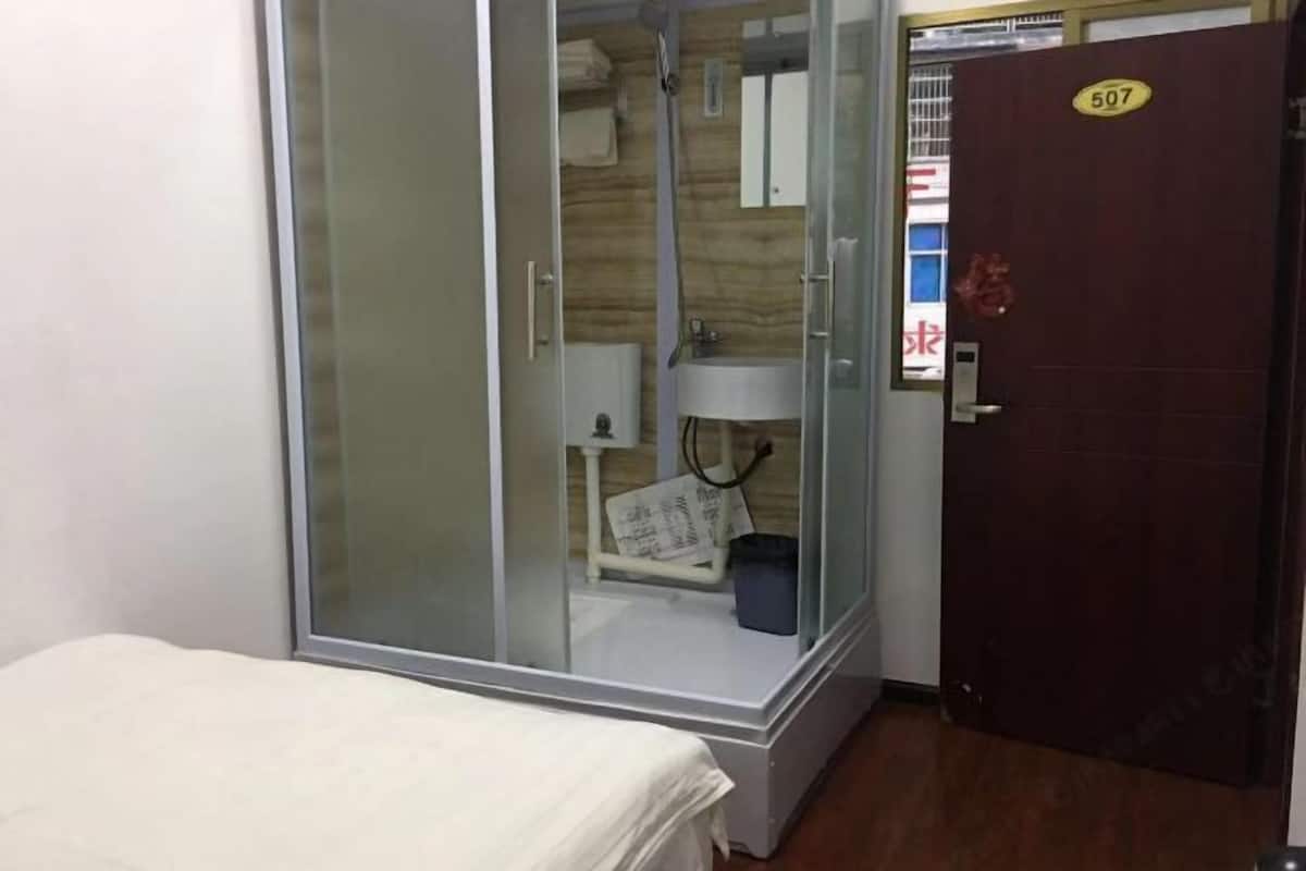 Une chambre comprenant un lit, une cabine de douche en verre, un lavabo et une porte portant le numéro 507.