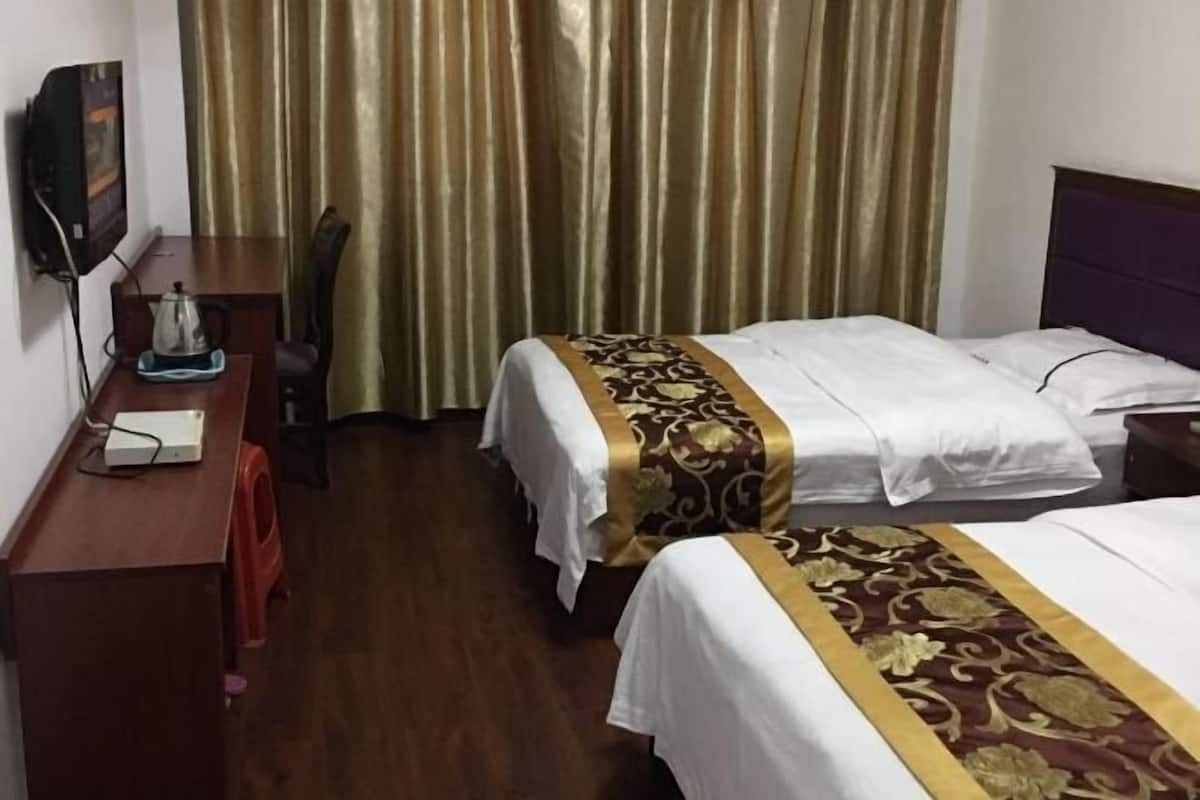 Une chambre d’hôtel avec deux lits, un bureau avec un ordinateur, une télévision et un rideau.
