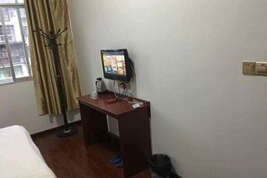Habitación de hotel con escritorio de madera, un monitor de computadora, ventana con cortinas, cama y un cesto de basura.
