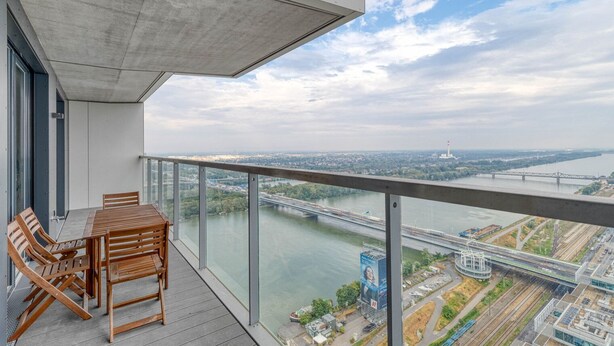 Een balkon met een tafel en stoelen, uitkijkend op een rivier en een brug.
