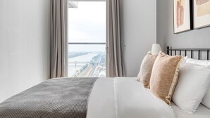 Een hotelkamer met een groot bed, uitzicht op een brug en stadsgezicht, en een gekaderd kunstwerk aan de muur.