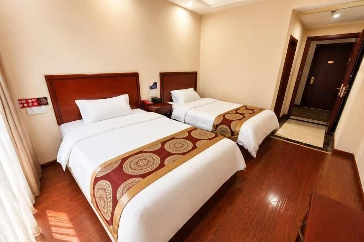 A hotel room with two beds, wooden headboards, a nightstand, a bedside table, and a door leading to a hallway.