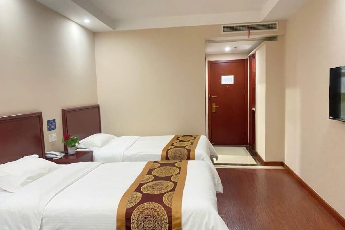 A hotel room with two beds, a TV, and a door leading to a hallway.