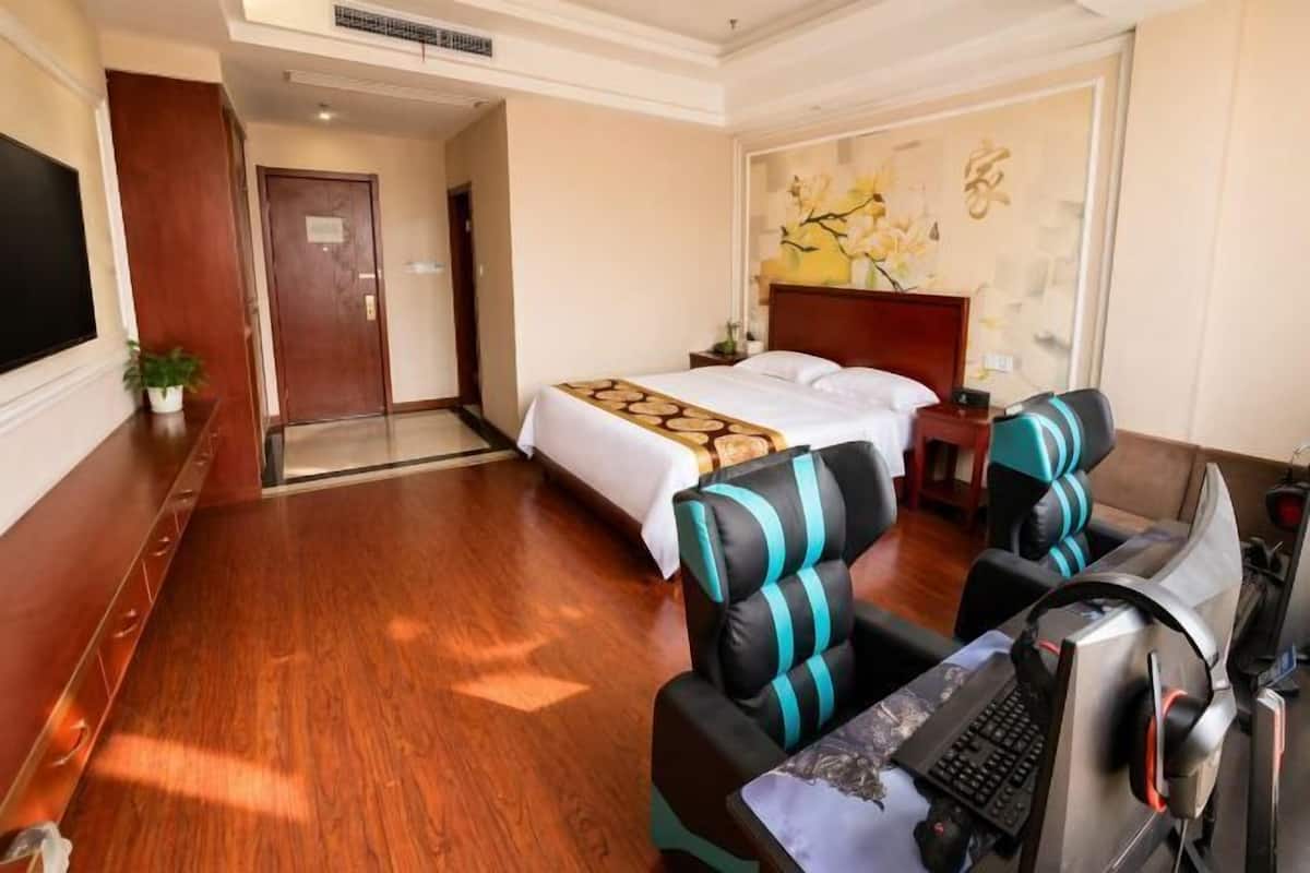 A hotel room with a bed, a desk with a computer, a chair, and a television.