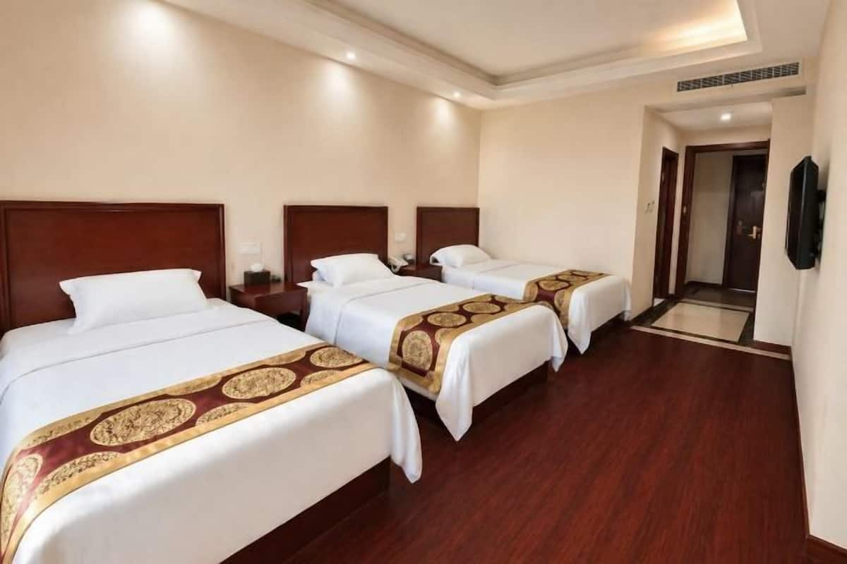 A hotel room with three beds, wooden flooring, and a television mounted on the wall.