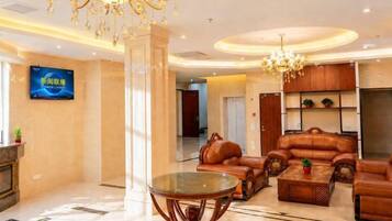 A hotel lobby with a chandelier, leather sofas, a coffee table, and a flat-screen TV.