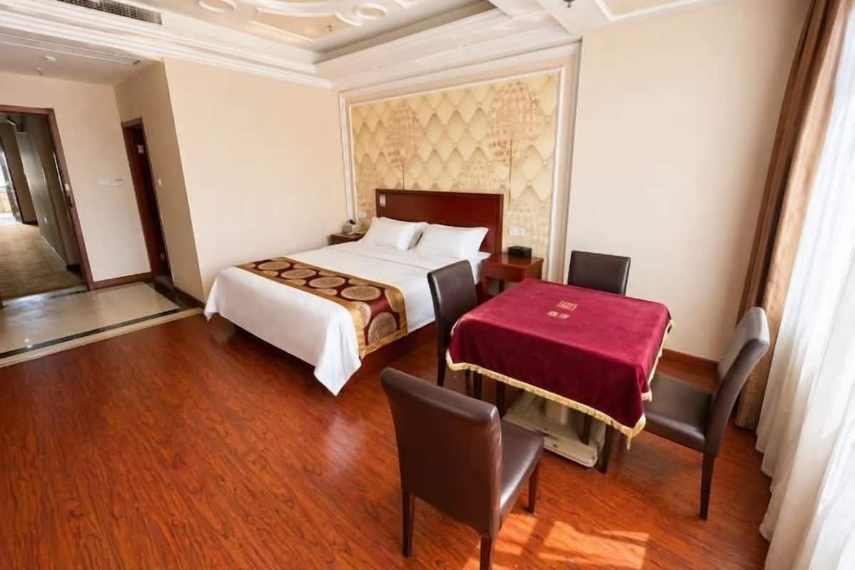 A hotel room with a bed, a dining table with chairs, and a wooden floor.