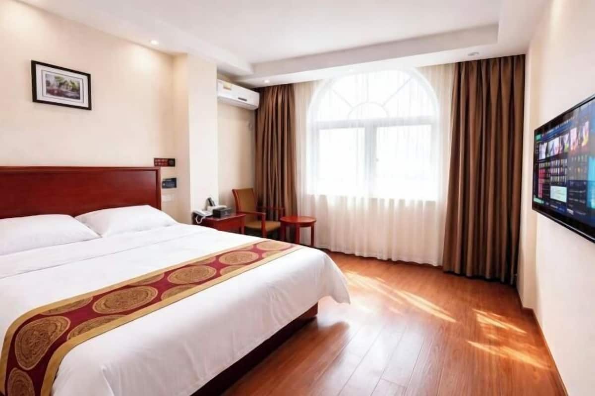 A hotel room with a large bed, a desk, a chair, a TV, and a window with curtains.