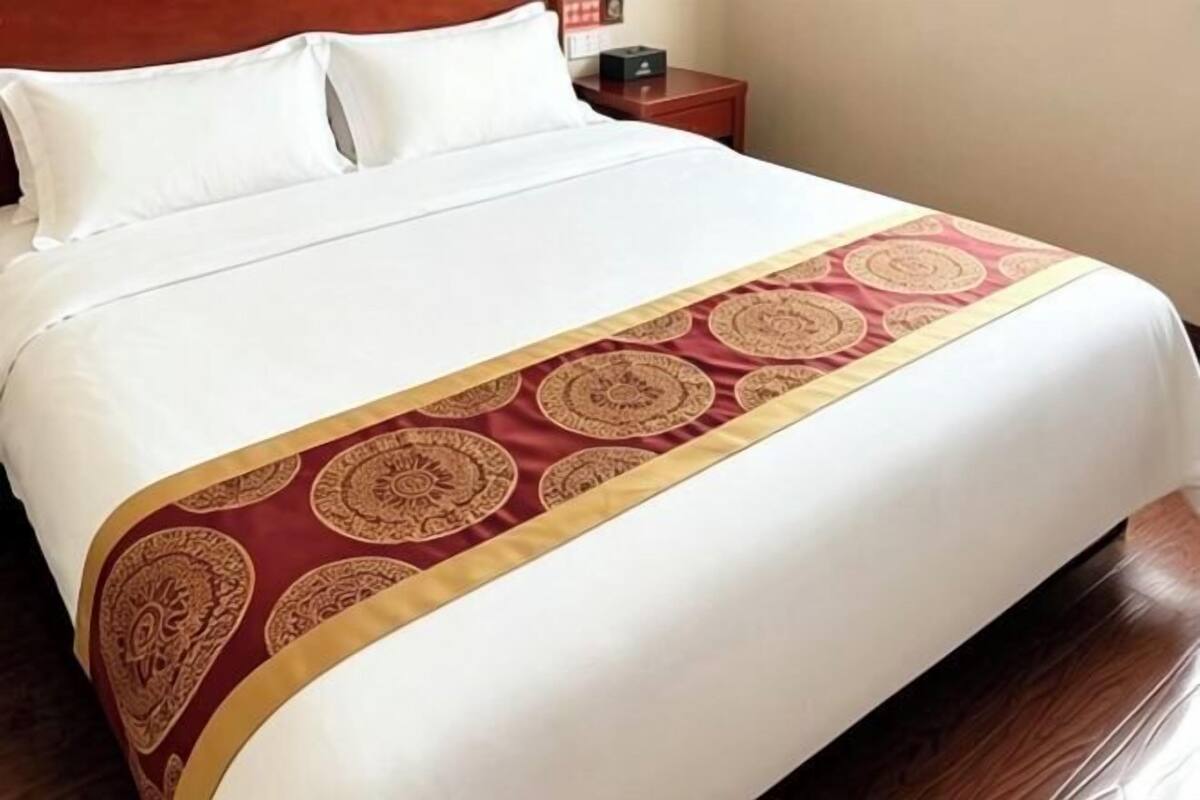 A bed with a white mattress and a red and gold patterned bedspread.