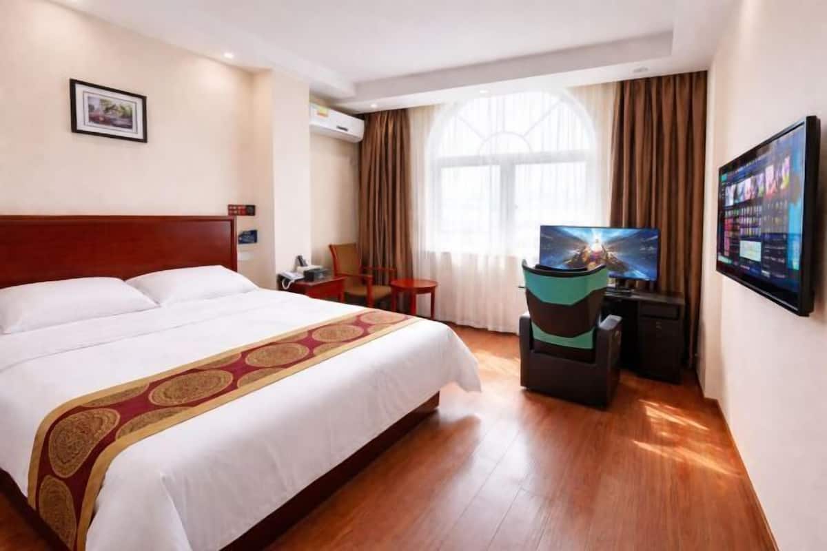 A hotel room with a large bed, a television, a desk, and a window with curtains.