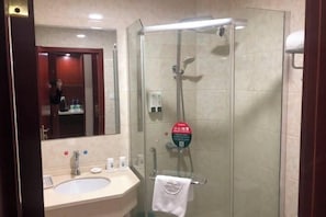 A bathroom with a glass-enclosed shower, a sink with a mirror, and toiletries on the counter.