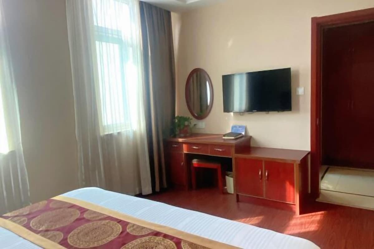 A hotel room with a bed, a desk, a chair, a television, and a wardrobe.